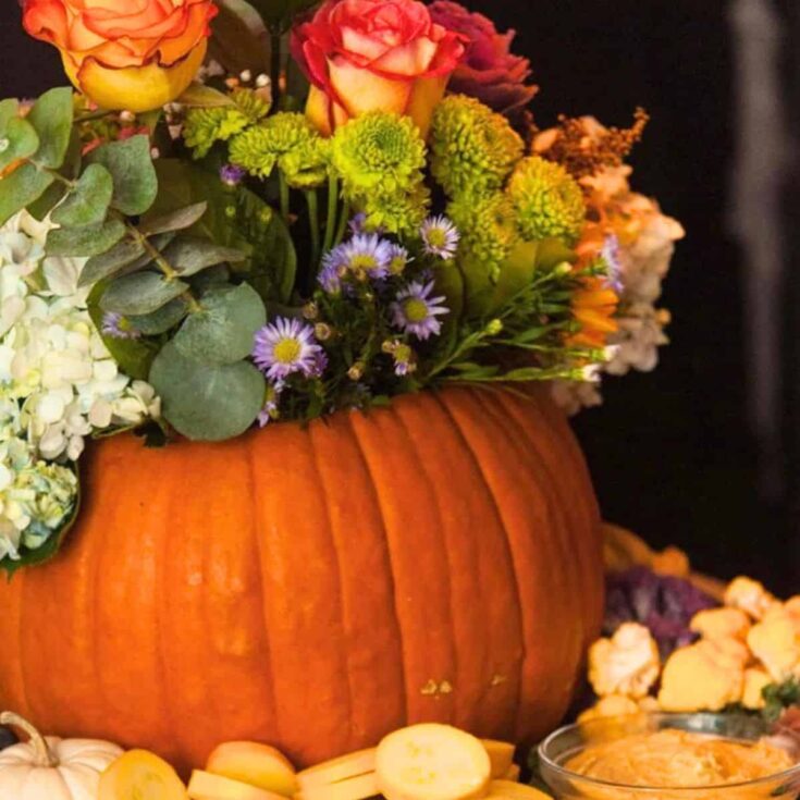 A pumpkin centerpiece with flowers with appetizers around it