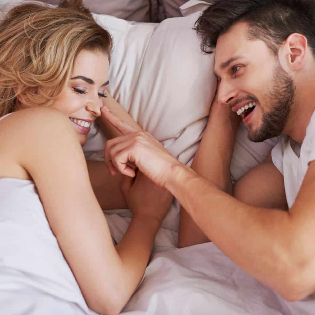 A happy couple in bed, the man pointing out the woman's nose