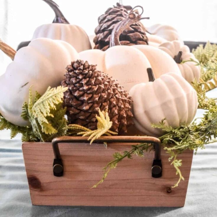 a fall table centerpiece made from a wooden box with white pumpkins and pinecones