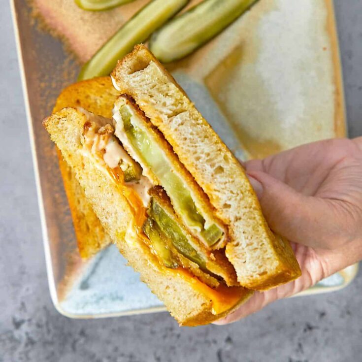 A person holding a fried green tomato grilled cheese sandwich