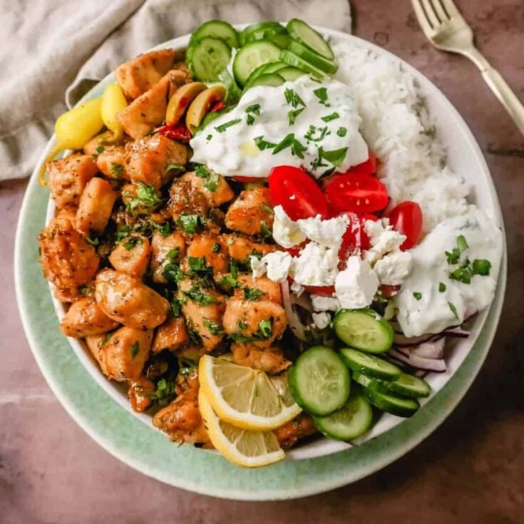 A bowl of Greek chicken with rice, lemon, cucumber