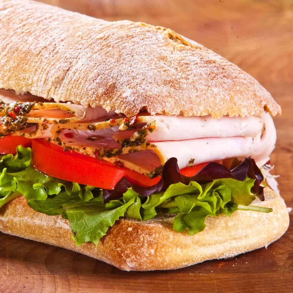 Sandwich made with rustic bread and layers of ham, lettuce, and tomato, made after reading these picnic sandwich recipes
