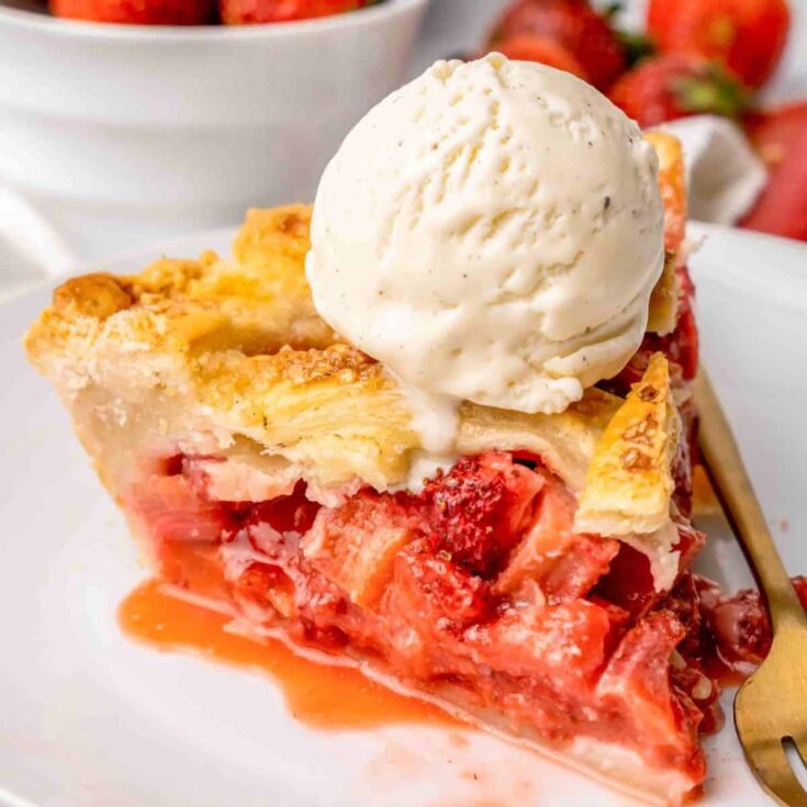 A slice of classic strawberry rhubarb pie topped with a scoop of ice cream