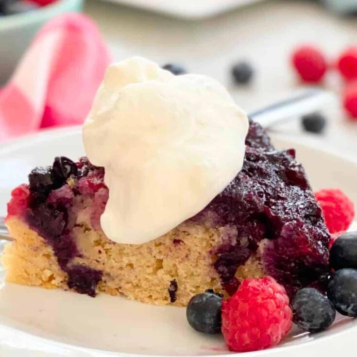 A slice of double berry upside down cake with blueberries and raspberries on the side