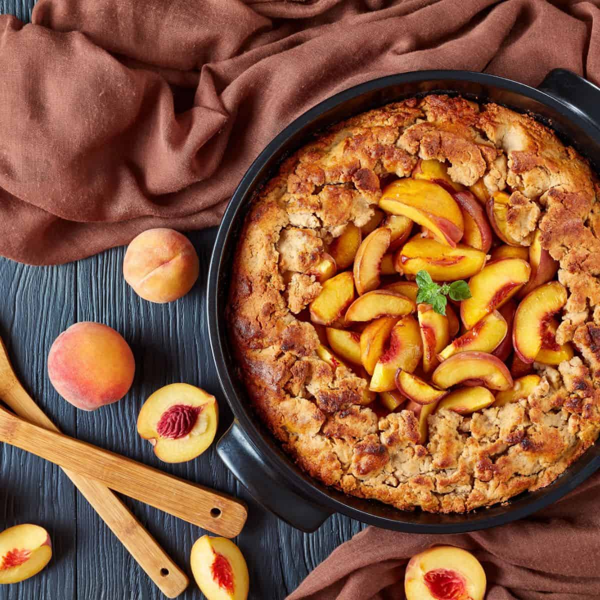 A top view of a peach cobbler as well as some fresh cut peaches, as one of these peach dessert recipes.