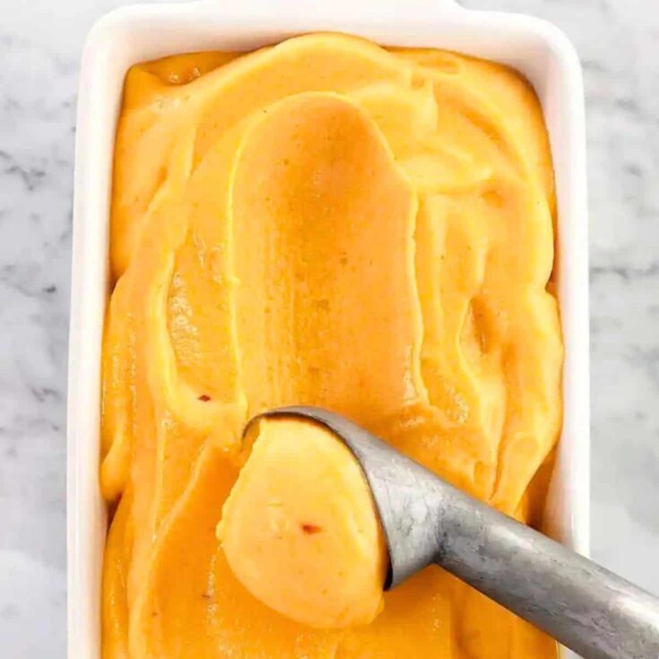 A person scooping a peach sorbet
