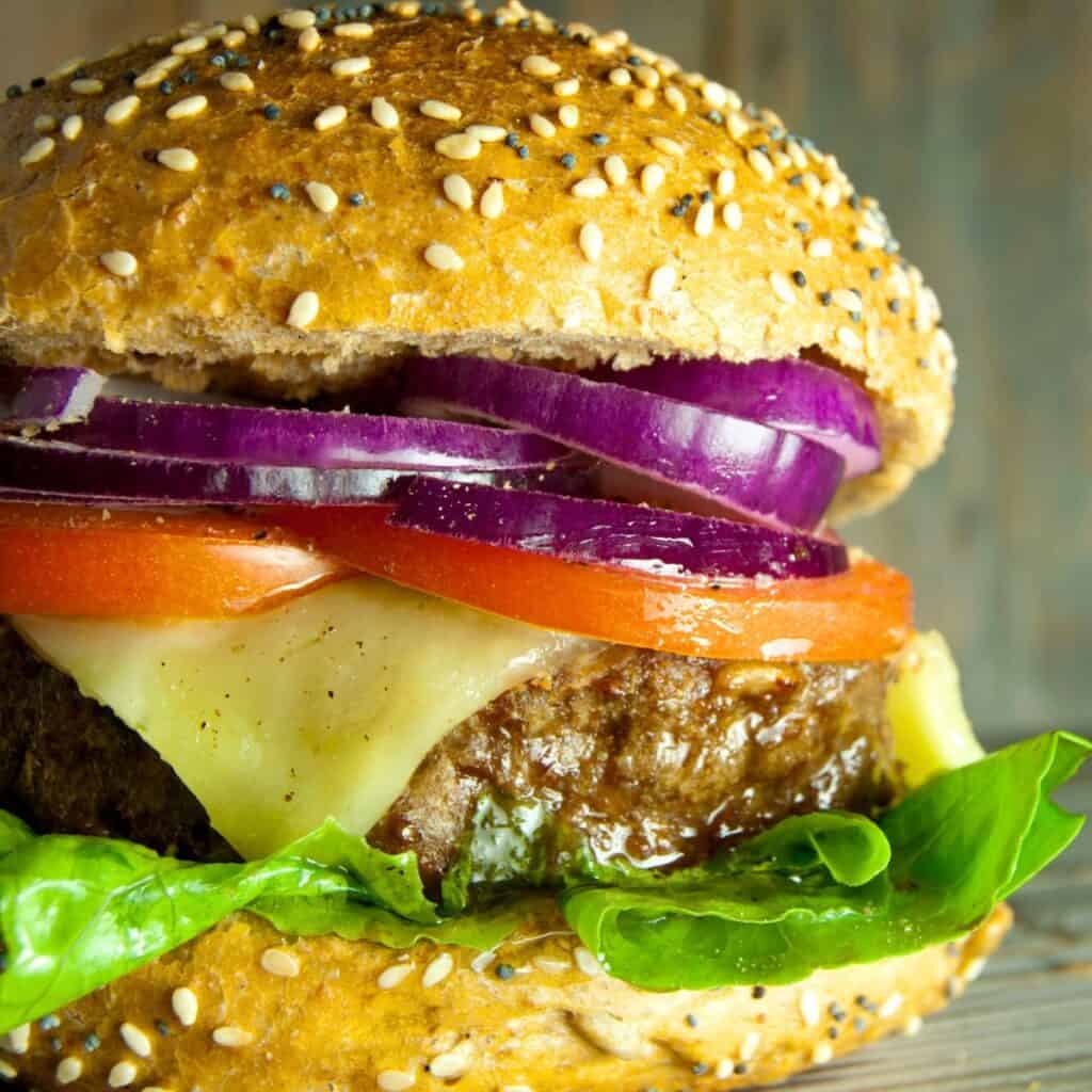 A burger layered with fresh lettuce, melted cheese, tomato, beef, and onions, made after reading these Burger recipes