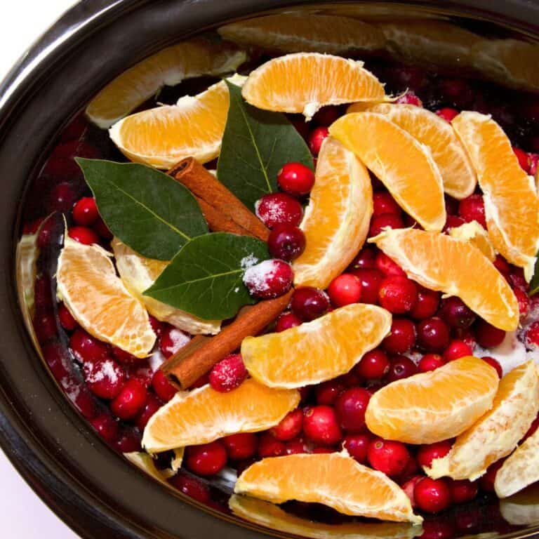 A slow cooker with ingredients including orange slices, cranberries, cinnamon sticks, and bay leaves, made after reading these Christmas crockpot recipes