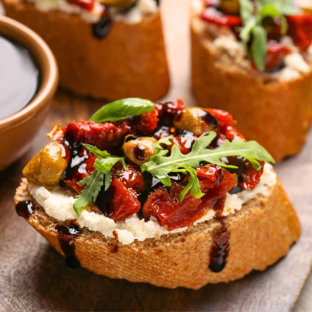 A plated dish of bruschetta, topped with ricotta, cream cheese, and red peppers, made after reading these one bite appetizers