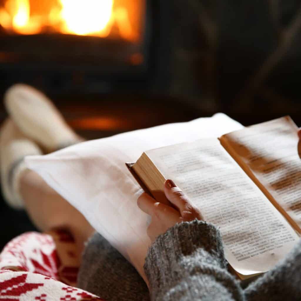 A woman reading a book by the fireplace