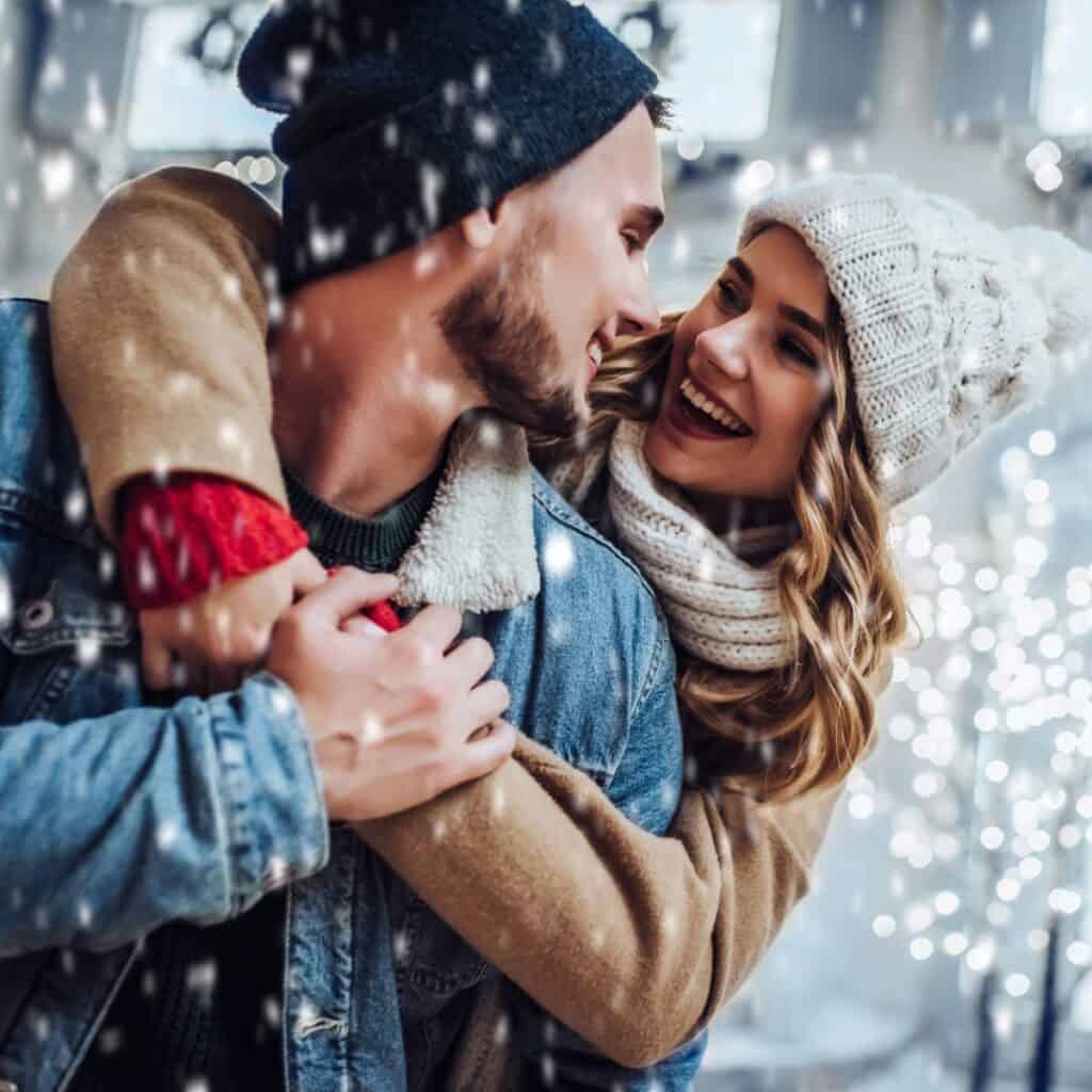 A happy couple looking at each other in the middle of a snow fall. New year's resolutions for couples