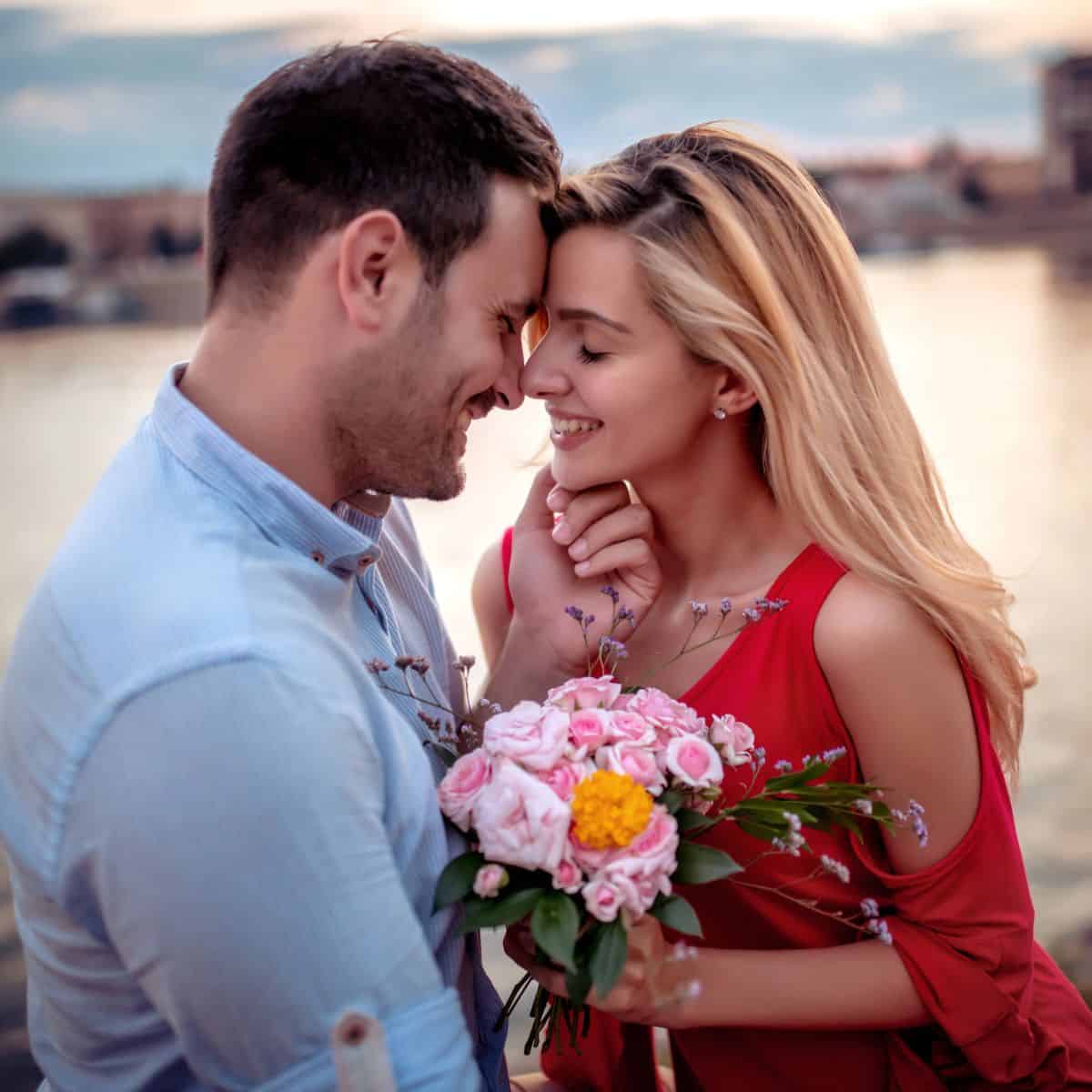 A couple by the lake, very close to each other, the woman holding her flowers gifted by her man, after reading these anniversary gift ideas