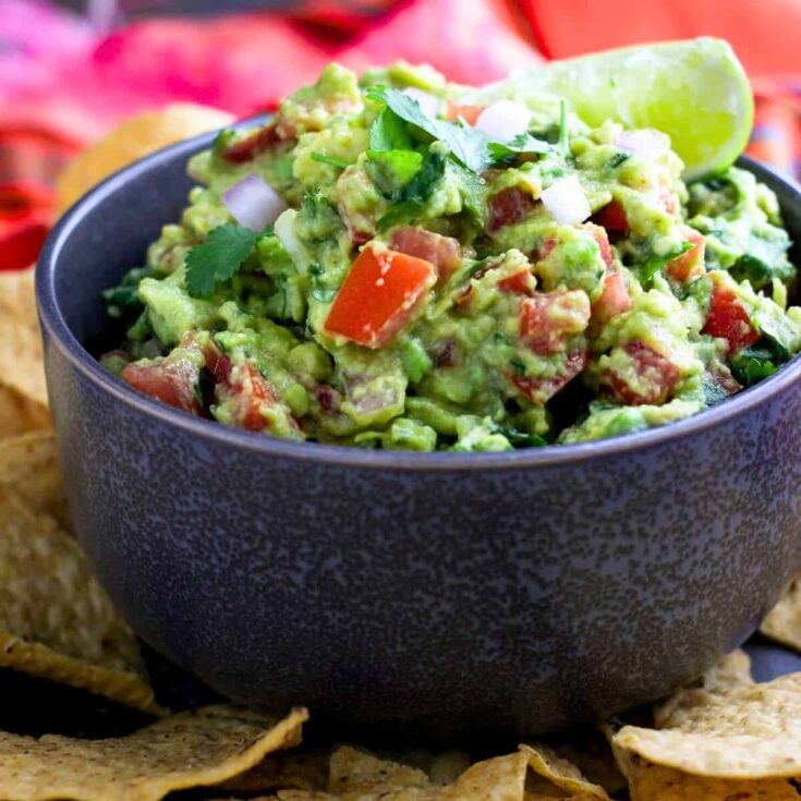 Spicy chunky guacamole in a bowl, with nachos on the side