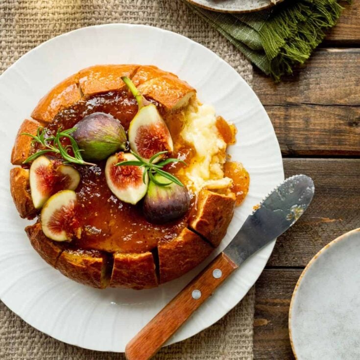 Bread bowl baked brie appetizer served on a plate, made after reading these Fall dinner party recipes